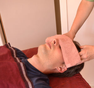 Praticienne qui masse la tête d'un client allongé sur la table de massage. Soin ayurveda