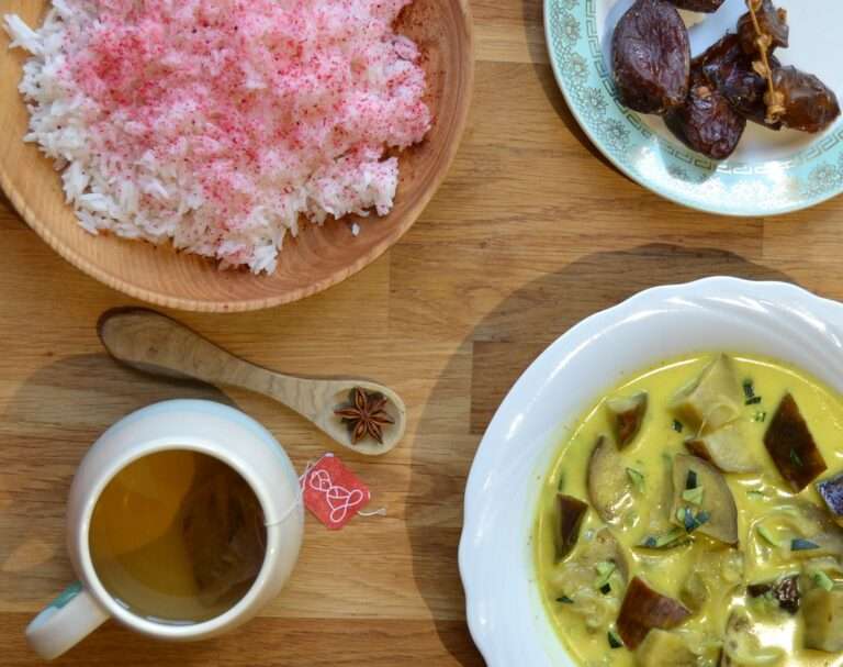 Assiettes vues par le haut : riz safrané, dattes, curry d'aubergines et coco. Une tasse de tisane Atma accompagne le repas