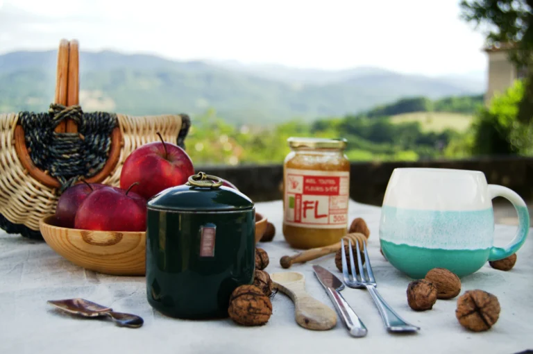 Des pommes, des noix, du miel, un pot de tisane, un panier pour la cueillette. Le paysage du Couserans au fond